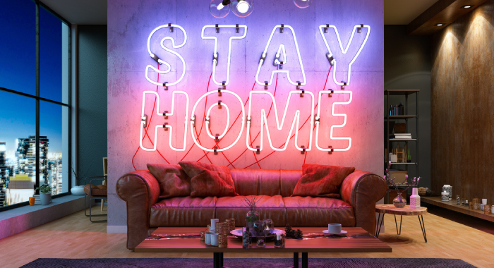 A couch with a neon sign behind it that says, "Stay Home."