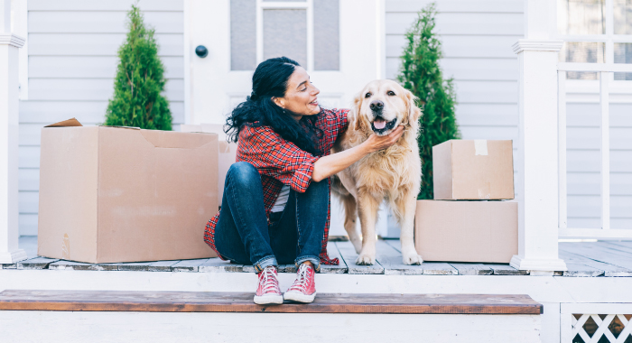 Woman sitting outside with her dog surrounded by moving boxes