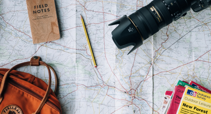 A camera, a bag, a notebook, a pen, and other items sitting on top of a map.