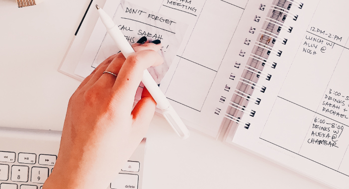 Person with a pen in hand looking at a planner