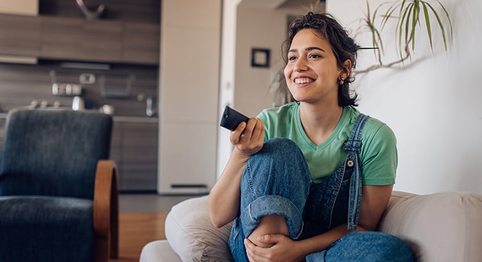 young person smiling and holding a remote control while sitting on a couch