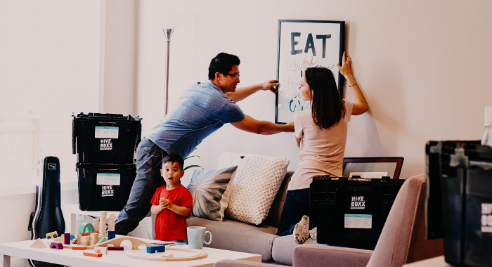 A family of three hanging a piece of artwork in their home