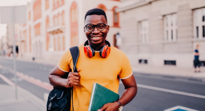 person with a backpack, notebook, and headphones smiling at the camera