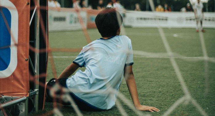 Child sitting on turf in front of a goal net