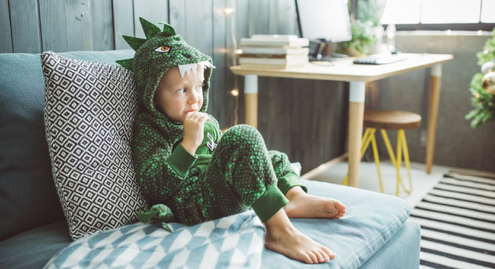 child with a dinosaur costume sitting on a bed