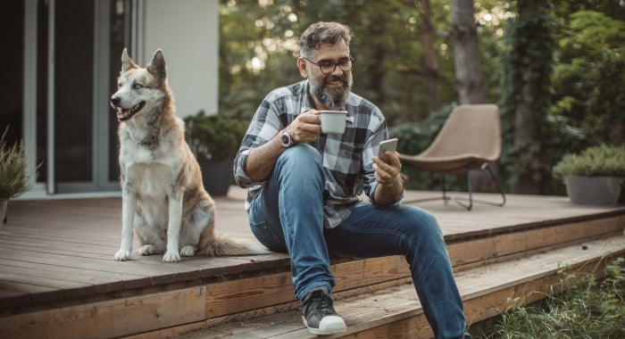 Man on his phone sitting with his dog on the porch.