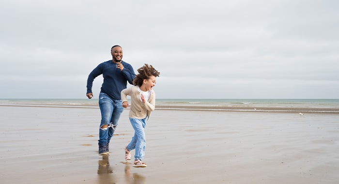 father running with his daughter along the beach on vacation